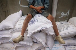 Palestinian child sits on top of sacks of flour at a United Nations Relief and Works Agency (UNRWA)